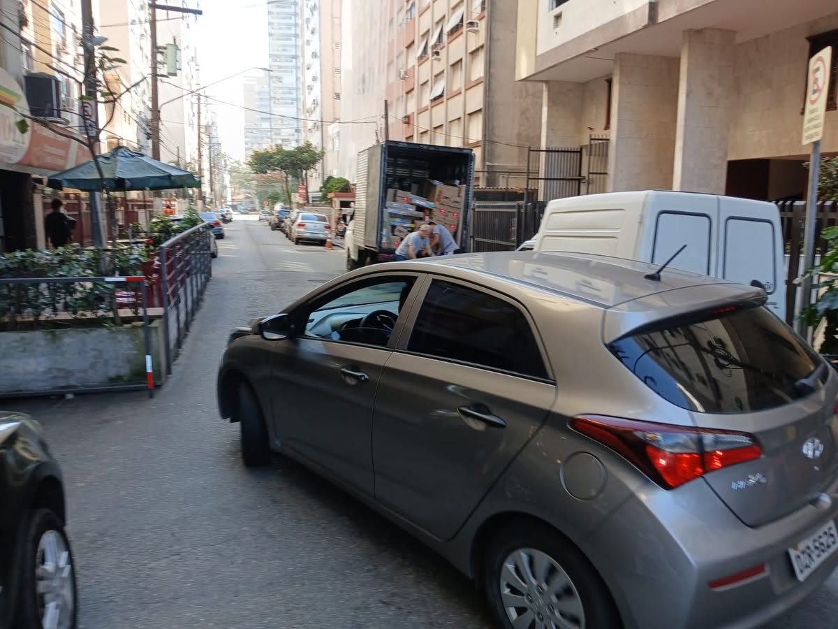 Caminhão em operação de carga e descarga e veículos disputando espaço na Rua Olavo Bilac, em Santos